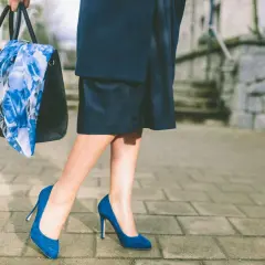 Elegancka kobieta w butach w kolorze szafirowym i granatowej spódnicy, niosąca torebkę z kwiecistym szalem.