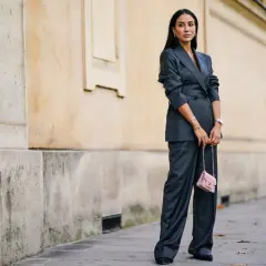 Elegancka kobieta w grafitowym garniturze, z różową torebką. Kolor gołębi jej stylizacji idealnie komponuje się z miejskim krajobrazem.