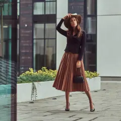 Elegancka kobieta w brązowej sukience i kapeluszu, zastanawia się, jakie buty do brązowej sukienki będą najlepsze.