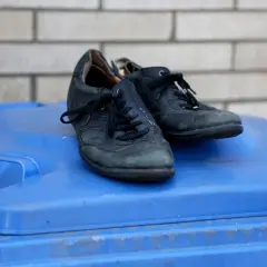 Para stare buty, gdzie wyrzucić? Czarne, skórzane buty leżą na niebieskim koszu na śmieci.