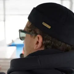 Mężczyzna w czarnej dokerce i okularach przeciwsłonecznych, patrzący w dal.