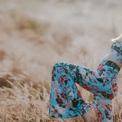 Blondynka w kwiecistym komplecie i okularach przeciwsłonecznych, uosobienie wolnego ducha i mody lat 70., pozuje na tle złocistego pola.