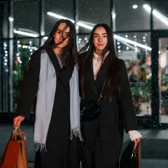 Dwie kobiety w płaszczach, z torbami na zakupy, w zimowej scenerii. Ich styl przypomina estetykę dark academia.