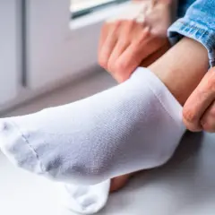 Ręce zakładają białą skarpetkę na stopę. Dowiedz się, jak wybielić skarpetki, aby były jak nowe.
