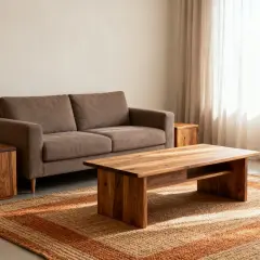 Sofa w kolorze taupe, czyli brązowo-szarym, obok drewnianych stolików i dywanu.