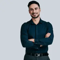 Uśmiechnięty mężczyzna w granatowej koszuli i szarych spodniach. Idealny zestaw: jakie spodnie do granatowej koszuli?