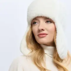 Kobieta w białym, puszystym nakryciu głowy z nausznikami, z blond włosami i delikatnym makijażem.