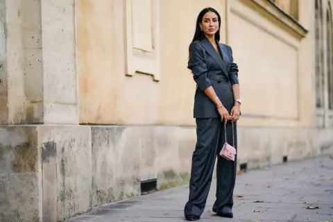 Elegancka kobieta w grafitowym garniturze, z różową torebką. Kolor gołębi jej stylizacji idealnie komponuje się z miejskim krajobrazem.