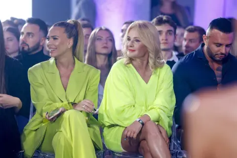 Dwie kobiety w stylizacjach w kolorze limonkowym siedzą w pierwszym rzędzie. Jedna w garniturze, druga w sukience.