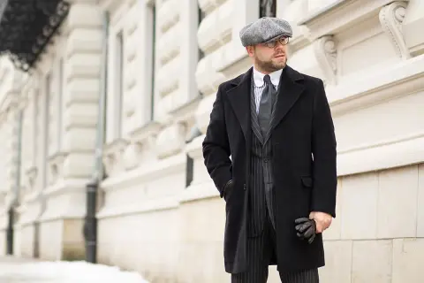 Elegancki mężczyzna w czapce i płaszczu, stylizacja inspirowana modą lat 40.