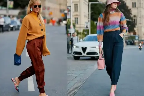 Dwie kobiety prezentują swoje stylizacje dnia, czyli ootd co to. Jedna w musztardowym kardiganie i brązowych spodniach, druga w kolorowym swetrze i granatowych spodniach.