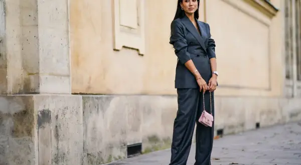 Elegancka kobieta w grafitowym garniturze, z różową torebką. Kolor gołębi jej stylizacji idealnie komponuje się z miejskim krajobrazem.