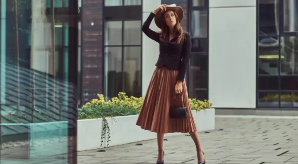 Elegancka kobieta w brązowej sukience i kapeluszu, zastanawia się, jakie buty do brązowej sukienki będą najlepsze.