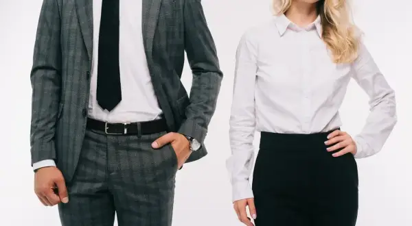 Elegancka para w strojach biznesowych. On w szarym garniturze w kratę, ona w białej koszuli i czarnej spódnicy. TPO.