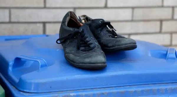 Para stare buty, gdzie wyrzucić? Czarne, skórzane buty leżą na niebieskim koszu na śmieci.