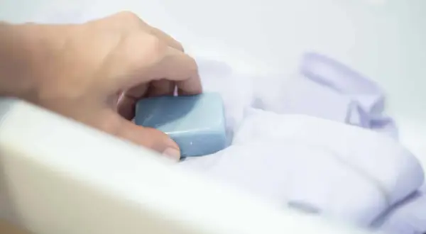 Ręka trzyma kostkę mydła nad białym materiałem. Mydło to skuteczny sposób, czym usunąć klej z tkaniny.