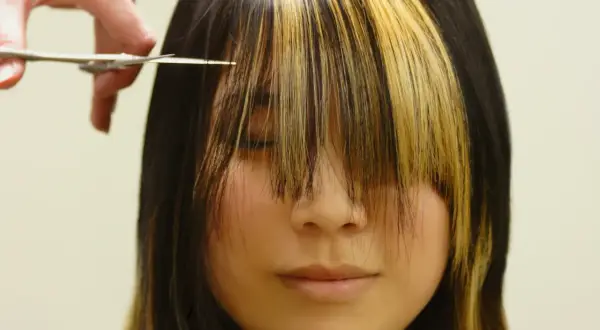 Fryzjerka przycina grzywkę w stylu birkin bangs. Dwukolorowe pasma opadają na twarz.