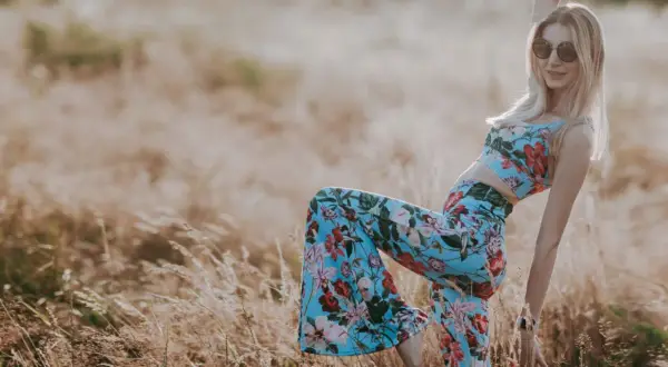 Blondynka w kwiecistym komplecie i okularach przeciwsłonecznych, uosobienie wolnego ducha i mody lat 70., pozuje na tle złocistego pola.
