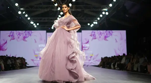 Modelka prezentuje suknię haute couture w kolorze pudrowego różu z falbanami na wybiegu.