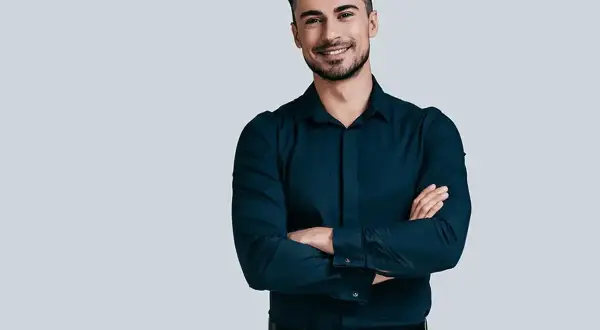 Uśmiechnięty mężczyzna w granatowej koszuli i szarych spodniach. Idealny zestaw: jakie spodnie do granatowej koszuli?