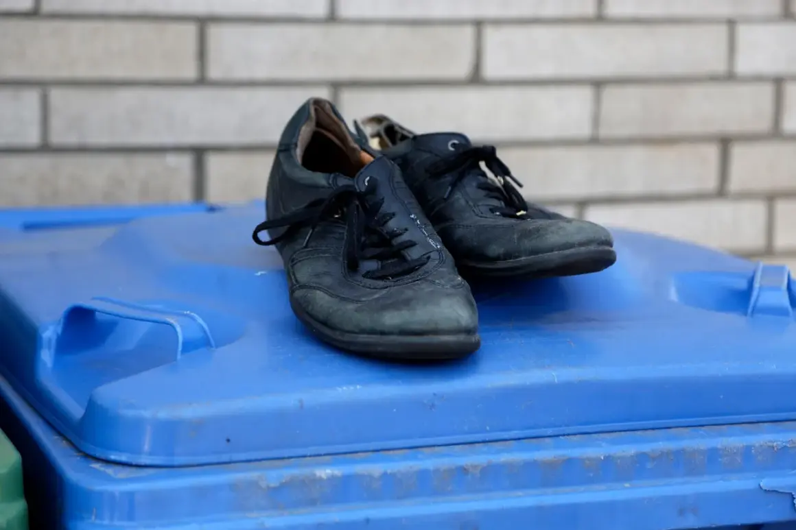 Para stare buty, gdzie wyrzucić? Czarne, skórzane buty leżą na niebieskim koszu na śmieci.