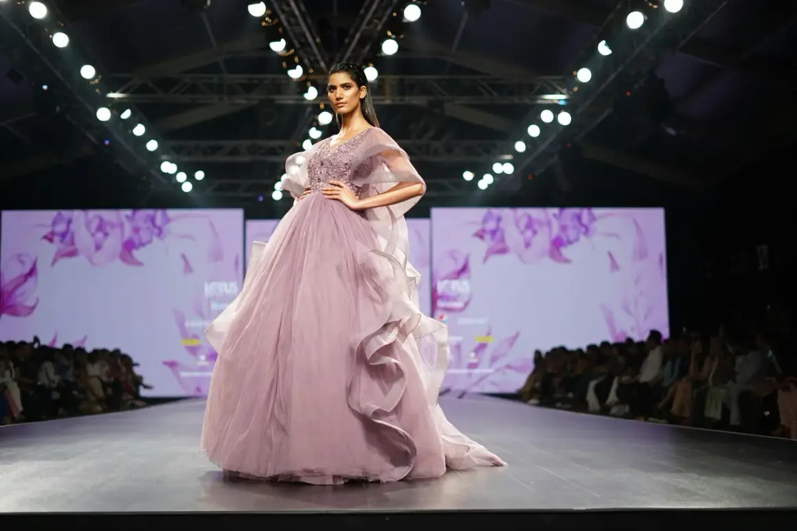 Modelka prezentuje suknię haute couture w kolorze pudrowego różu z falbanami na wybiegu.
