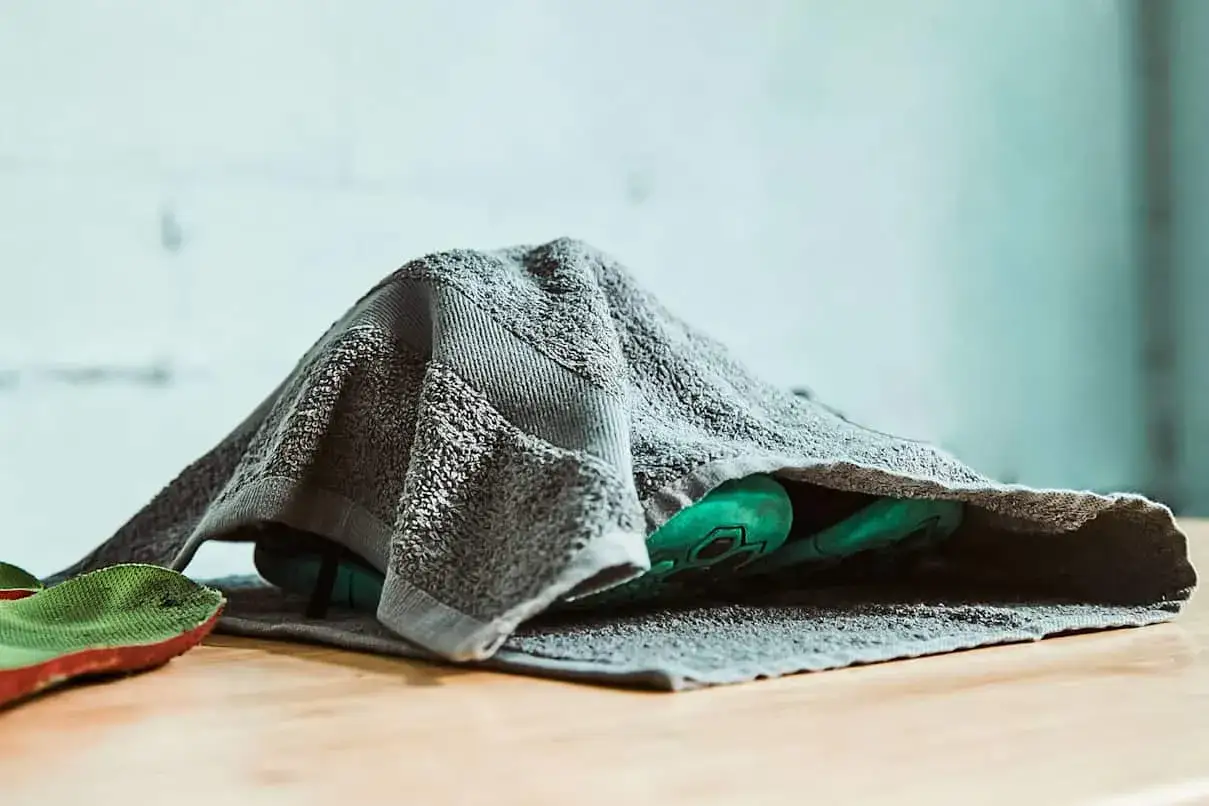 Zielone buty pod szarym ręcznikiem. Szybko wysuszyć buty? Ten sposób działa!
