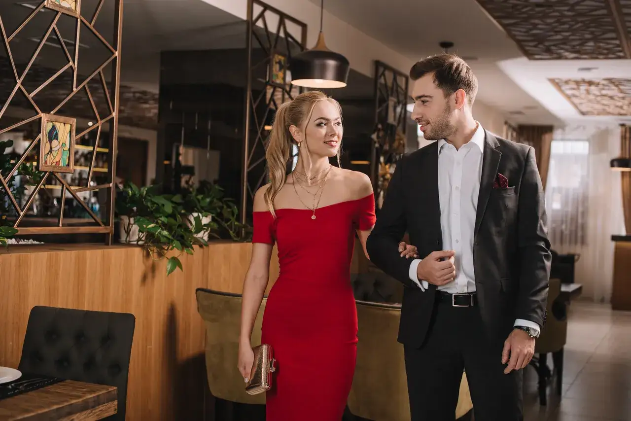 Para elegancko ubrana para w stylu cocktail attire idzie przez restaurację. Ona w czerwonej sukience, on w garniturze.