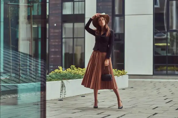 Elegancka kobieta w brązowej sukience i kapeluszu, zastanawia się, jakie buty do brązowej sukienki będą najlepsze.
