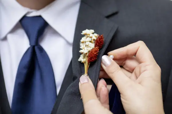 Dłoń przypina do marynarki delikatną brustaszę z suszonych kwiatów.